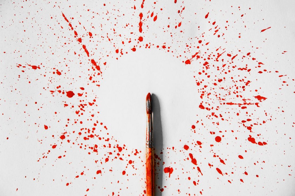 Pinceau taché de peinture rouge posé sur une feuille blanche, entouré d'éclaboussures de peinture formant un motif éclaté.